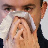 Hombre joven con un pañuelo de papel sonándose la nariz
