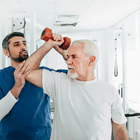 Hombre mayor levanta una mancuerna ayudado por un sanitario