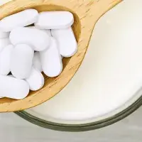 Pastillas blancas en una cuchara de madera sobre un vaso de leche