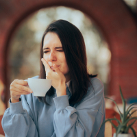 Mujer joven con hipersensibilidad dental tomando una bebida en una taza
